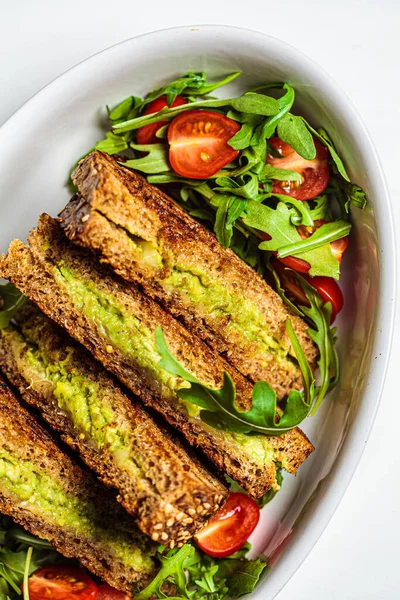 Grilled avocado and cheese sandwiches with fresh salad in a white dish. Healthy snack concept.