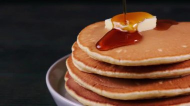 Koyu arkaplanda tereyağı ve akçaağaç şurubu olan krep yığını, kapat.