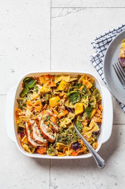 Fırında sebzeli Farfalle makarna ve beyaz tabakta tavuk, gri arka plan..