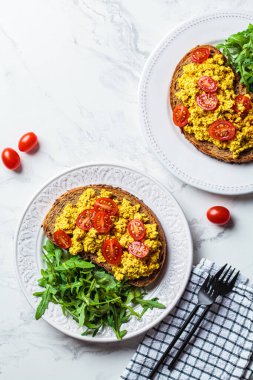 Domatesli çırpılmış tofu tostu ve beyaz bir tabakta roka, beyaz mermer arka plan..