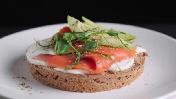 Tostadas de desayuno con queso, salmón y aguacate, fondo negro. — Vídeo de stock