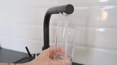 Mutfaktaki musluktan bardağa su dökün, beyaz fayanslar arka planda..