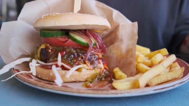 Weibliche Hände essen Burger mit Pommes in einem Restaurant, in Großaufnahme. Fastfood-Konzept. — Stockvideo