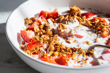 Granola with yogurt and strawberries in a white bowl, close-up. Healthy breakfast concept.