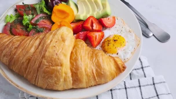 Placa de desayuno con croissant, aguacate, huevo frito y fruta, cámara lenta. — Vídeos de Stock