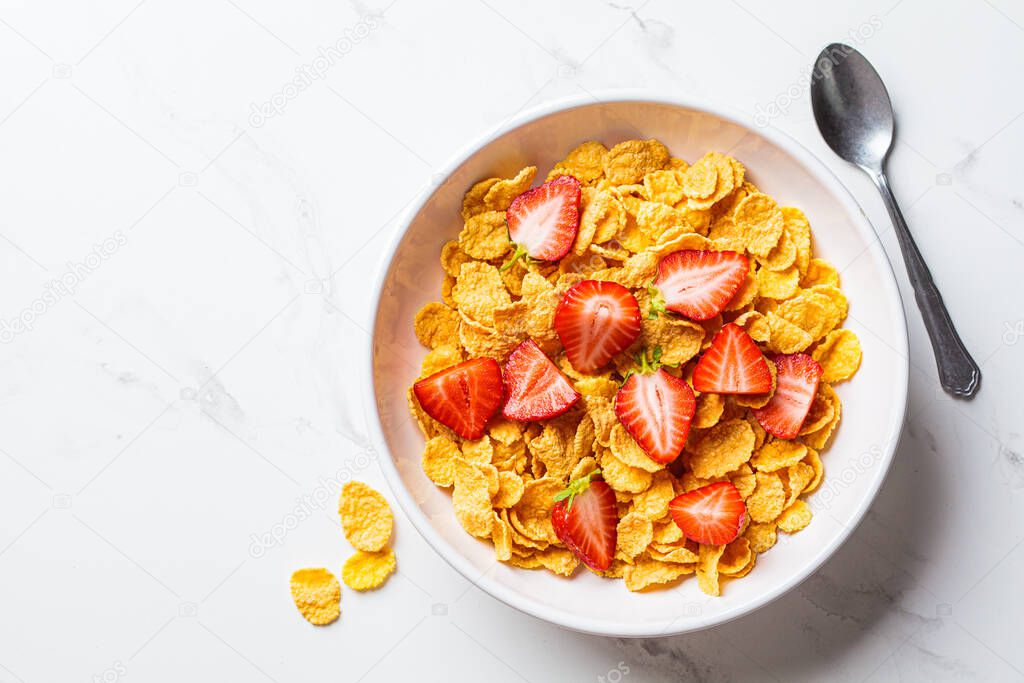 Cornflakes cereals with strawberries in a white bowl, top view. Healthy breakfast concept.