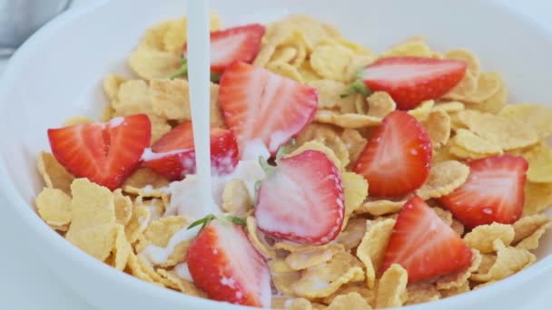 Milk is pouring into cornflakes with strawberries, slow motion. — Stock Video