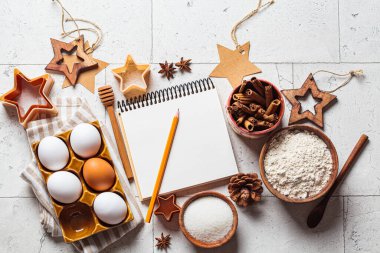 Noel pişirme konsepti. Gri fayanslı Noel kurabiyeleri için malzemeler, kopyalama alanı. Un, yumurta, şeker, tarçın ve yemek tarifi defteri, üst görünüm.
