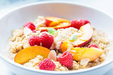 Ahududu, şeftali ve fındıklı yaz yulaf ezmesi, yakın plan. Sağlıklı vejetaryen gıda konsepti.