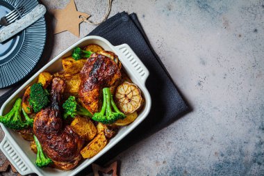 Fırında fırında tavuk budu, patates, brokoli ve sarımsaklı fırın tabağı, karanlık noel arkaplanı, fotokopi alanı. Sağlıklı yiyecek konsepti.