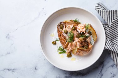 Whole baked potato stuffed with salmon, yogurt sauce and capers, top view.