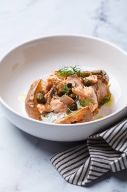 Whole baked potato stuffed with salmon, yogurt sauce and capers, close-up..