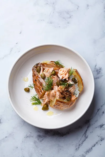Whole baked potato stuffed with salmon, yogurt sauce and capers, top view.