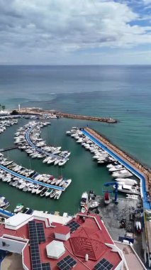 İspanya 'nın Dehesa de Campoamor bölgesindeki Akdeniz kıyısındaki yat marinasına bakan İHA görüntüsü. Açık deniz ve arka planda ufuk olan eğimli rıhtımlarda düzenlenmiş tekneler ve eğlence yatları..
