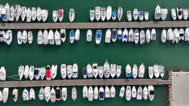 İspanya 'nın Akdeniz kıyısındaki bir marinada demirli tekne ve yatların insansız hava aracı görüntüleri. Temiz yeşil su manzarası, ahşap rıhtım ve modern eğlence tekneleri.. 