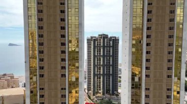 Benidorm 'daki modern gökdelenlerin arka planında deniz olan insansız hava aracı görüntüsü. Açık bir günde yukarıdan çekilen yüksek altın binalar ve konut kuleleri.