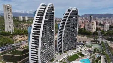 Camdan balkonları ve çağdaş mimarisi olan iki modern eğimli yerleşim yerinin hava aracı görüntüleri. Arka planda şehir binaları, yollar ve yeşil alanlar görülüyor. 