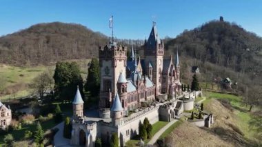 Güneşli bir günde yeşil tepeler ve ormanlarla çevrili tarihi kuleleri ve dekoratif mimarisi olan Drachenburg Kalesi 'nin insansız hava görüntüsü..