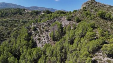 Açık güneşli bir günde Akdeniz kırsalında çam ormanı, kayalık tepeler ve yeşil vadilerle çevrili dağ köyünün insansız hava aracı görüntüsü