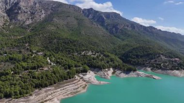 Turkuaz dağ gölü, kayalık kıyı şeridi, yeşil orman tepeleri ve dramatik arazi huzurlu doğa ve seyahat manzarası yaratıyor.
