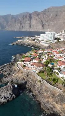 Los Gigantes 'in Tenerife' deki insansız hava görüntüsü dramatik uçurumlarla doğal okyanus havuzu kayalık sahil şeridi tatil köyleri ve derin mavi Atlantik Okyanusu.