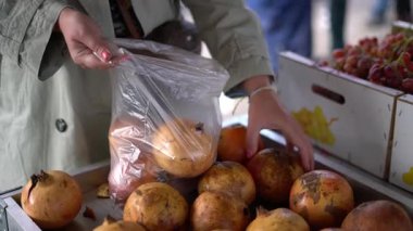 Taze nar seçen ve yerel bir çiftçi pazarında plastik torbaya koyan bir kadına yakın durun. Sağlıklı gıda alışverişi ve taze meyve kavramı.