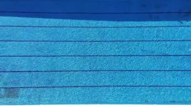 Güneşli bir günde, boş bir yüzme havuzunun mavi suları ve yüzme yolları olan insansız hava aracı görüntüsü. Yukarıdan temiz bir tatil havuzu görünüyor.