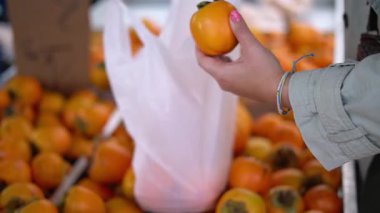 Yerel bir markette olgun hurma meyveleri seçen bir insanın eli, taze portakal ürünleri arasında plastik bir torba tutarak yakınlaşır.