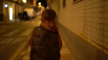 Küçük bir çocuğun gece sıcak sokak ışıklarıyla şehir kaldırımında zıplaması sakin bir şehir akşam atmosferi yaratıyor.