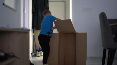 Yaratıcı bir DIY aktivitesi sırasında evde karton bir kutu oluşturmak için yapıştırıcı kullanan genç bir çocuk motor beceriler ve hayal gücü geliştiriyor.