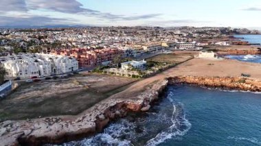 İspanya 'nın Torrevieja kıyı şehrinin insansız hava aracı görüntüsü kayalık kıyı şeridi binaları mavi deniz ve gün batımında kentsel manzara