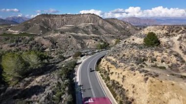 Güneşli bir günde İspanya 'da, kuru tepeler ve doğal manzaralar arasında dolambaçlı bir dağ yolu boyunca giden motorsikletin insansız hava görüntüsü.