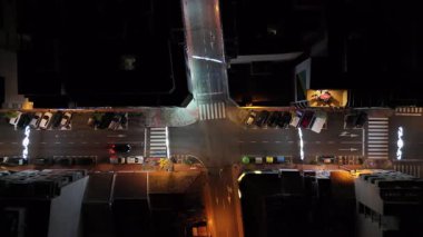 Geceleri şehir içi kavşağın tepeden aşağı hava aracı görüntüsü. Arabalar, yaya geçitleri, yol işaretleri ve şehir ışıkları geometrik şehir desenleri yaratıyor.