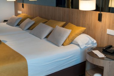 Rahat, modern otel odasının içi, düzgün yapılmış yatak odaları, yumuşak yastıklar, ahşap yatak başlığı ve sıcak lamba ışığı konaklama konsepti.