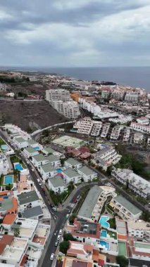 Los Gigantes yerleşim yerinin insansız hava görüntüsü villaları, yüzme havuzları, tenis kortu ve bulutlu gökyüzünün altındaki Atlantik okyanus kıyıları.