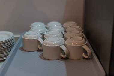 Beyaz seramik kahve fincanları ve tabaklar otel kahvaltısında ya da yemek alanında dizilmiştir. Minimum konukseverlik hizmeti ve içecek hazırlama konsepti temizdir.