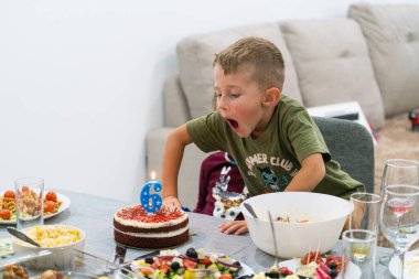 Doğum günü pastasında altı numaralı mumu söndüren sevimli küçük çocuk evde yemek ve aile ortamında sıcak bir kutlama yapıyor.
