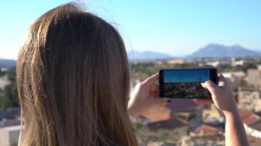 Şehir manzarası ve dağları akıllı telefondan kaydeden kadının arka görüntüsü. Seyahat videoları, şehir silueti, güneşli bir gün, modern mobil teknoloji.