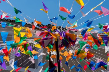 Parlak renkli parti bayrakları ve mavi gökyüzünün altında sokağın üzerinde asılı kiraz kuşu. Açık hava festivali dekorasyonu, kutlama ve yaz tatili atmosferi.