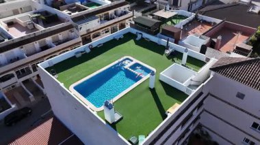 Açık yüzme havuzlu, yeşil bahçeli ve yaz tatili emlak yaşam tarzlı güneşli konut dairelerinin insansız hava aracı görüntüsü.
