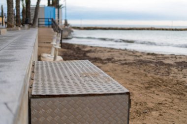 Sahil kenarındaki kumsalın yanında metal platform ve arka planda sakin deniz..