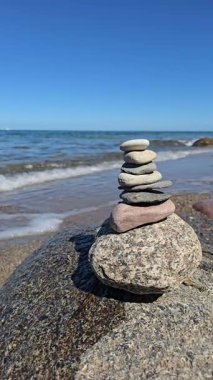 Dengeli taş yığını kayalık sahilde deniz dalgaları ve mavi gökyüzü huzurlu zen meditasyon konsepti uyumu farkındalık ve rahatlama.