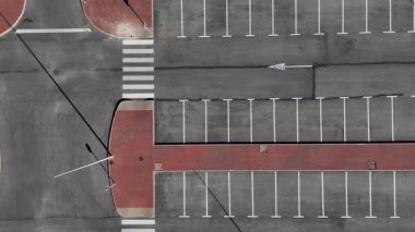 Beyaz yol işaretli, yaya geçidi ve asfalt kaldırımlı boş park alanının insansız hava aracı görüntüsü geometrik kentsel desen oluşturur.