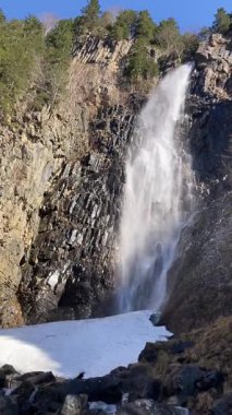Eşsiz kaya oluşumları ve bazalt sütunları üzerinden akan yüksek bir şelalenin çarpıcı bir görüntüsü. Kışın veya ilkbaharın başlarında mavi bir gökyüzü altında vahşi doğa tarafından çevrelenmiş. Trabzon Türkiye 'de Asmasu Şelalesi.