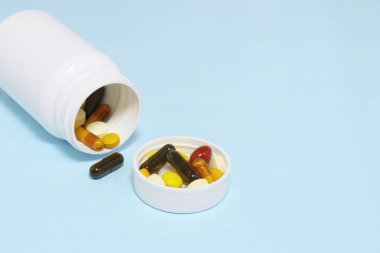 Mavi arka planda beyaz bir şişe ile vitamin ve takviyelerin yakın plan fotoğrafı. Buna multi vitaminler, B vitamini, C vitamini, D vitamini, kolajen hapları, probiyotik kapsüller ve demir kapsüller dahil..