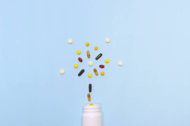 Vitaminlerin ve takviyelerin beyaz bir şişeyle mavi arkaplandaki en iyi görüntüsü. Buna multi vitaminler, B vitamini, C vitamini, D vitamini, kolajen hapları, probiyotik kapsüller ve demir kapsüller dahil..