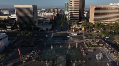 Long Beach şehir merkezinin geniş hava manzarası, CA binaların, dairelerin ve aktif demiryolu hatlarının üzerinden uçuyor. Okyanus ve kıyı şeridi ufuk çizgisinin ötesindeki şehri çevreledi..