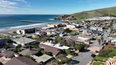 Kaliforniya, Cayucos 'un yükseltilmiş hava perspektifi rıhtım, kumlu plaj, okyanus dalgaları, yayalar, otlak arazi ve şehir merkezindeki sahil topluluğu yakınlarındaki 1. Otoyol' u gösteriyor..