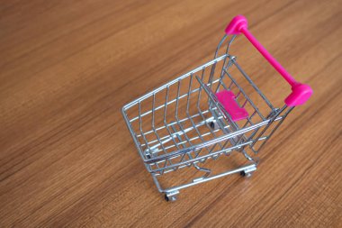 Shopping cart on wooden table on white background. Empty grocery shopping cart trolley. Copy space. Commerce concept