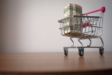 Pink handle shopping cart full of one dollar bills on wooden table. One dollar bills in a shopping basket